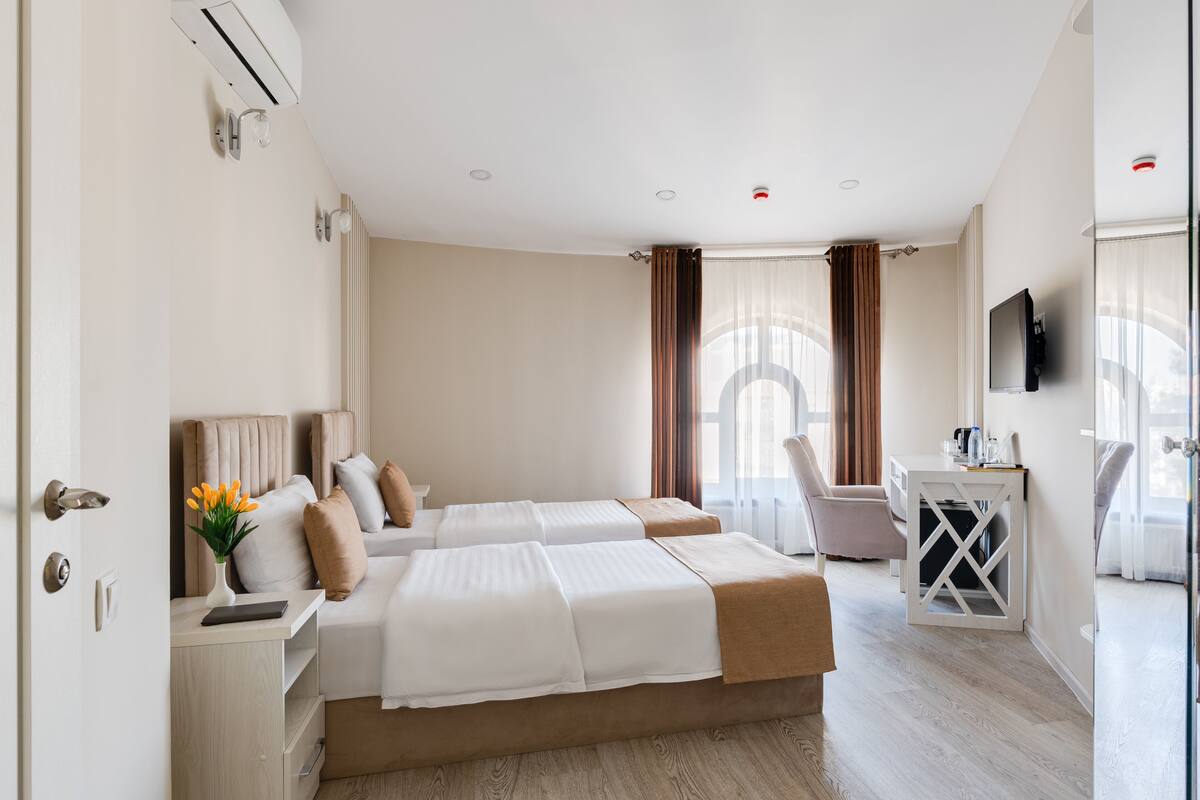 A hotel room with two beds, a desk, a chair, and a TV.