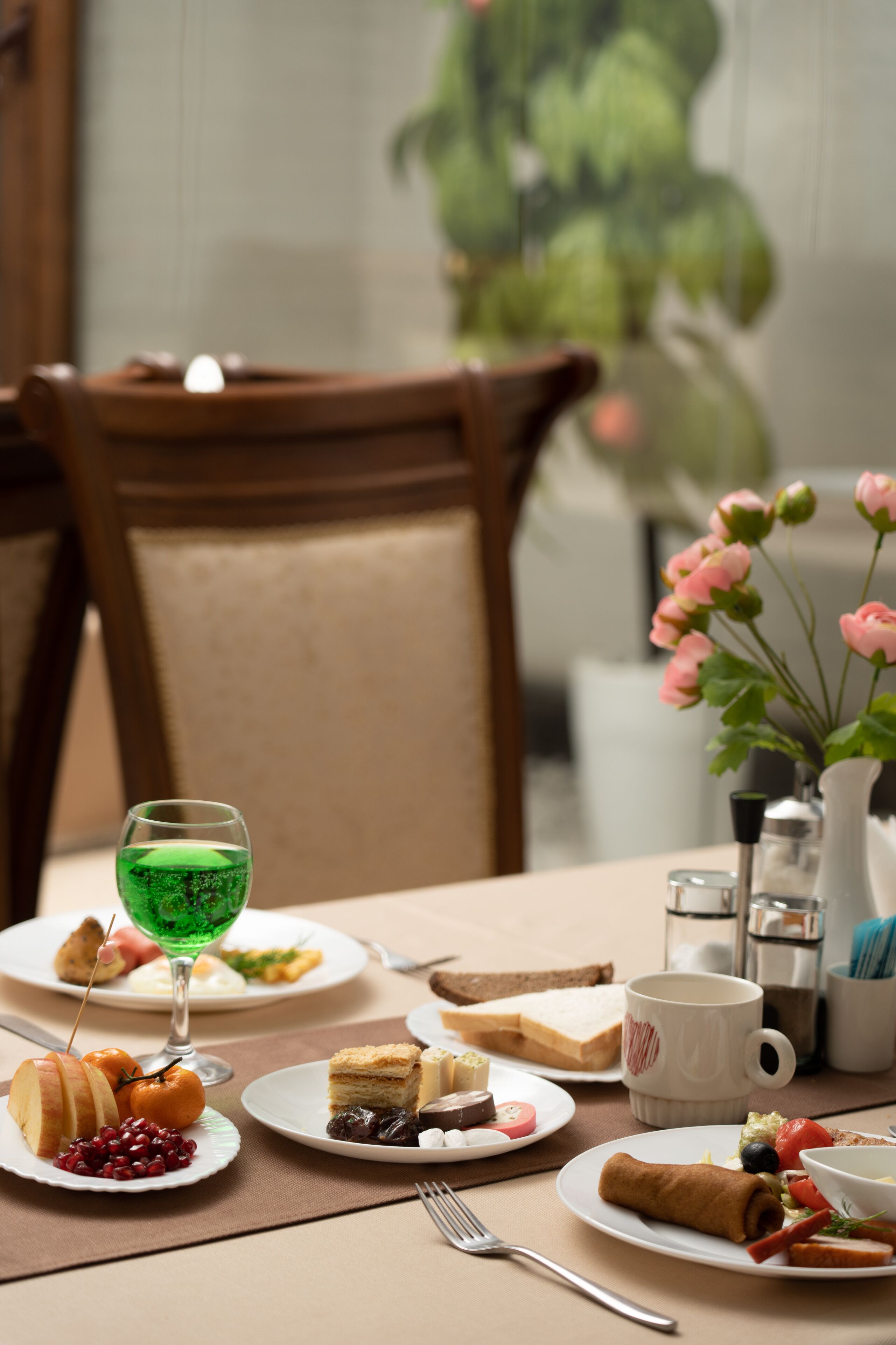 Una mesa de comedor con platos de comida, un vaso de bebida verde y un jarrón con flores rosas.