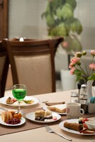 Una mesa de comedor con platos de comida, un vaso de bebida verde y un jarrón con flores rosas.