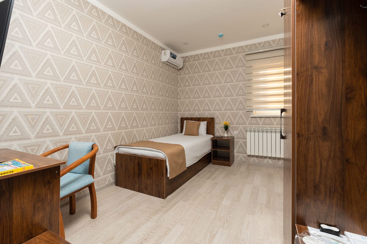 A bedroom with a bed, a desk, a chair, a nightstand, and a radiator.