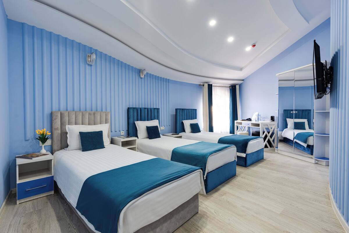A hotel room with three beds, a desk, and a mirror.