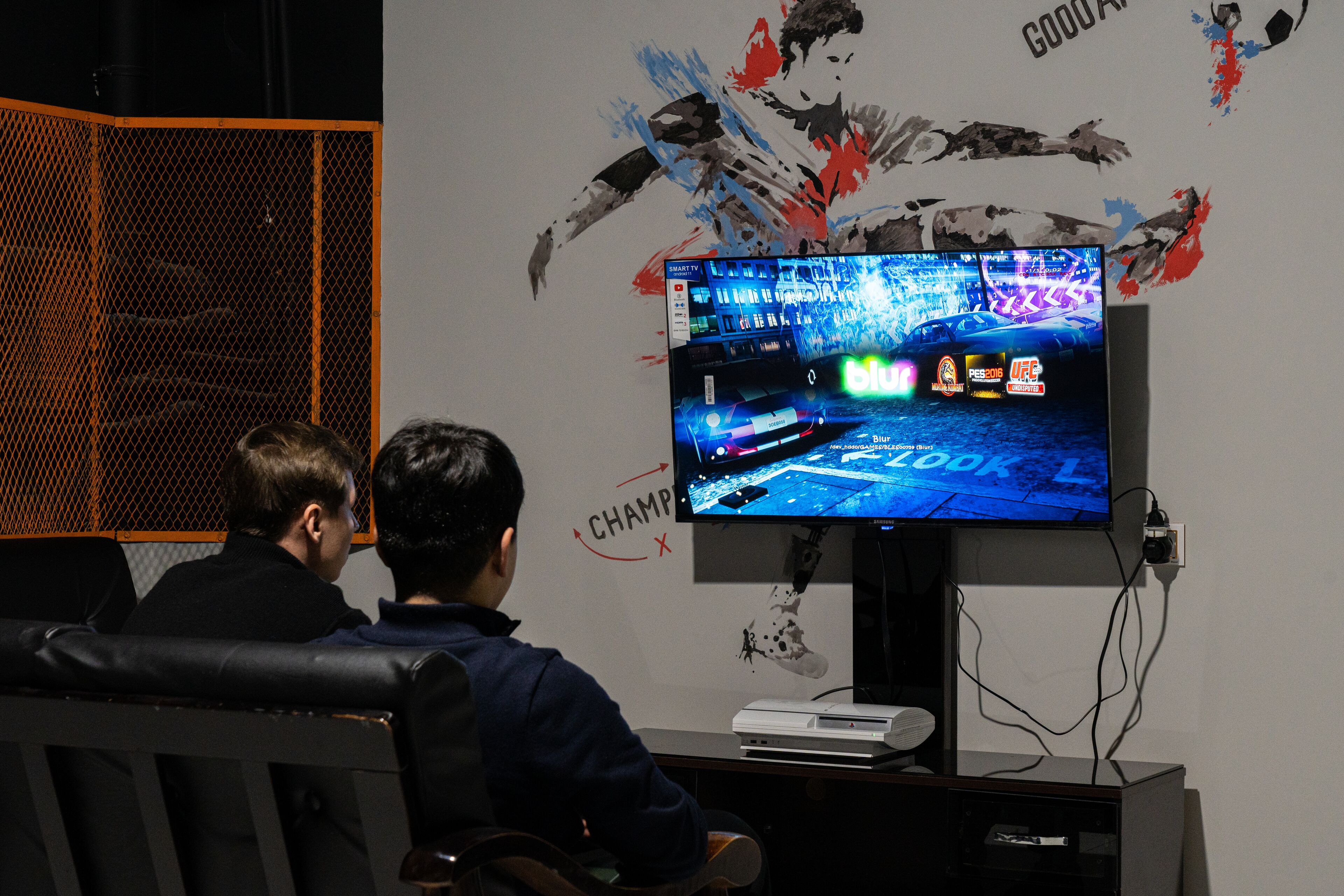 Une pièce dotée d’un grand écran diffusant un jeu vidéo, d’un espace détente avec des fauteuils et d’un mur orné d’œuvres d’art abstrait.