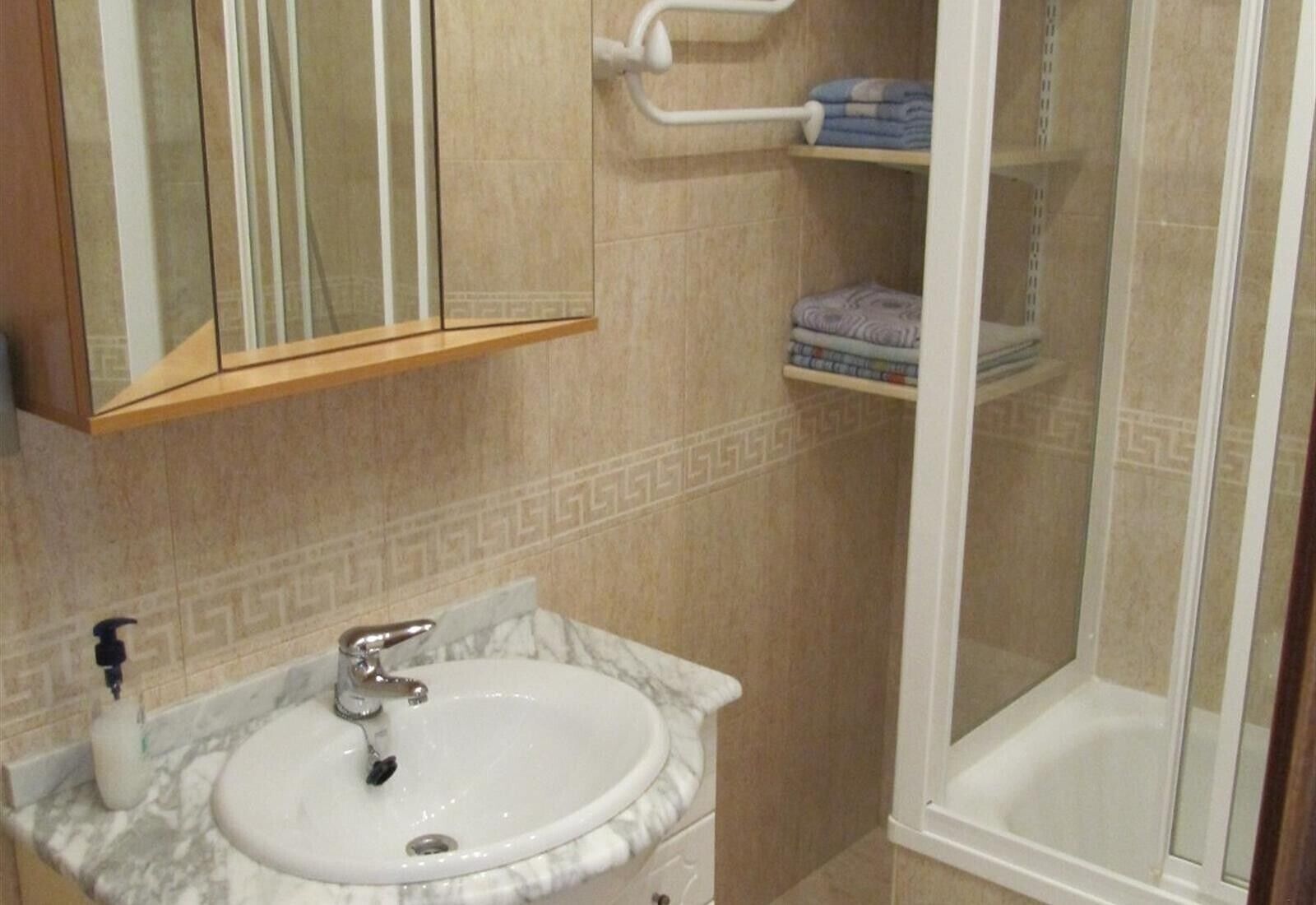 A bathroom with a marble sink, a glass shower enclosure, and a towel rack with folded towels.