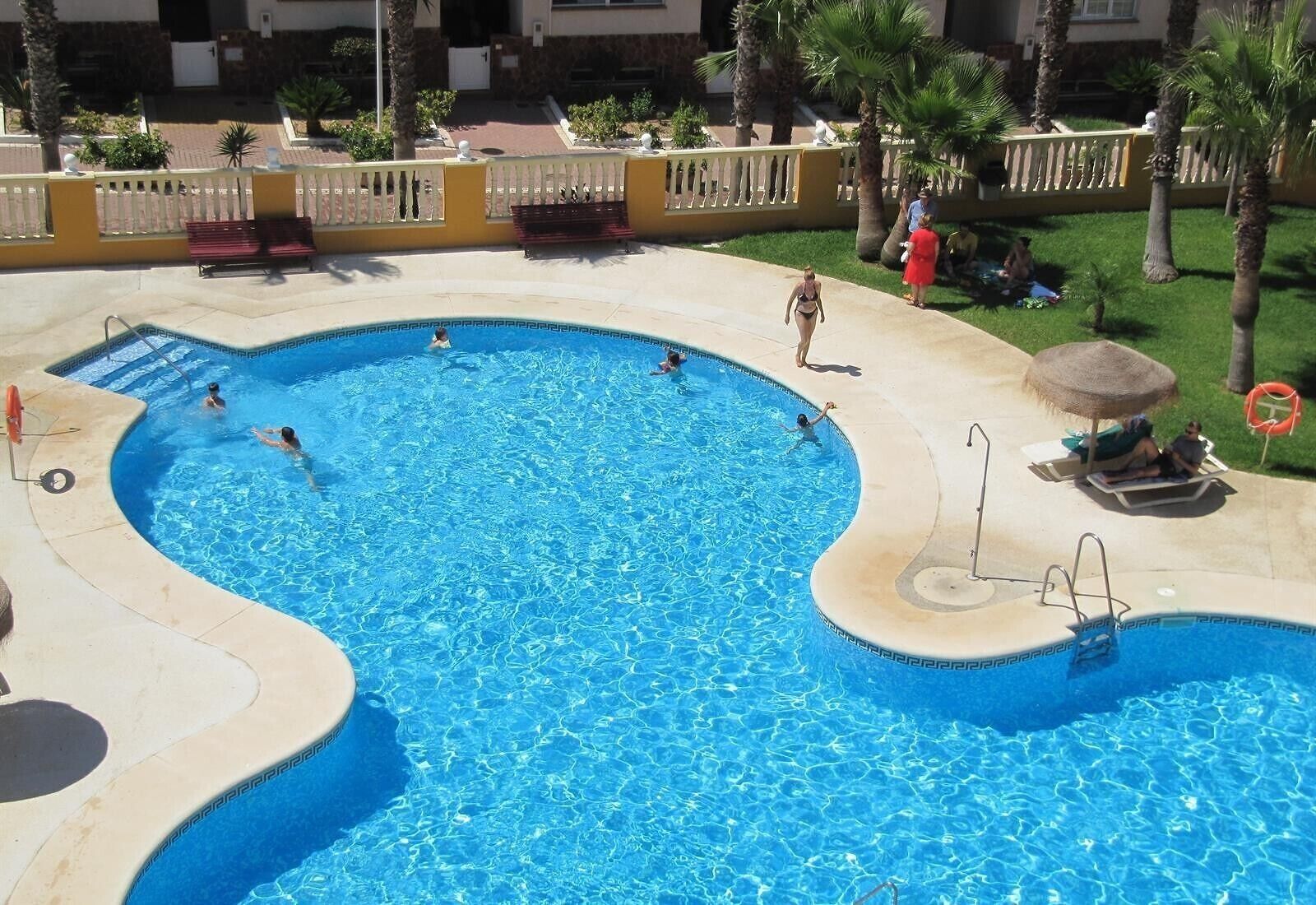 Una amplia piscina al aire libre con varias pistas de natación, un toldo y un puesto de socorristas.