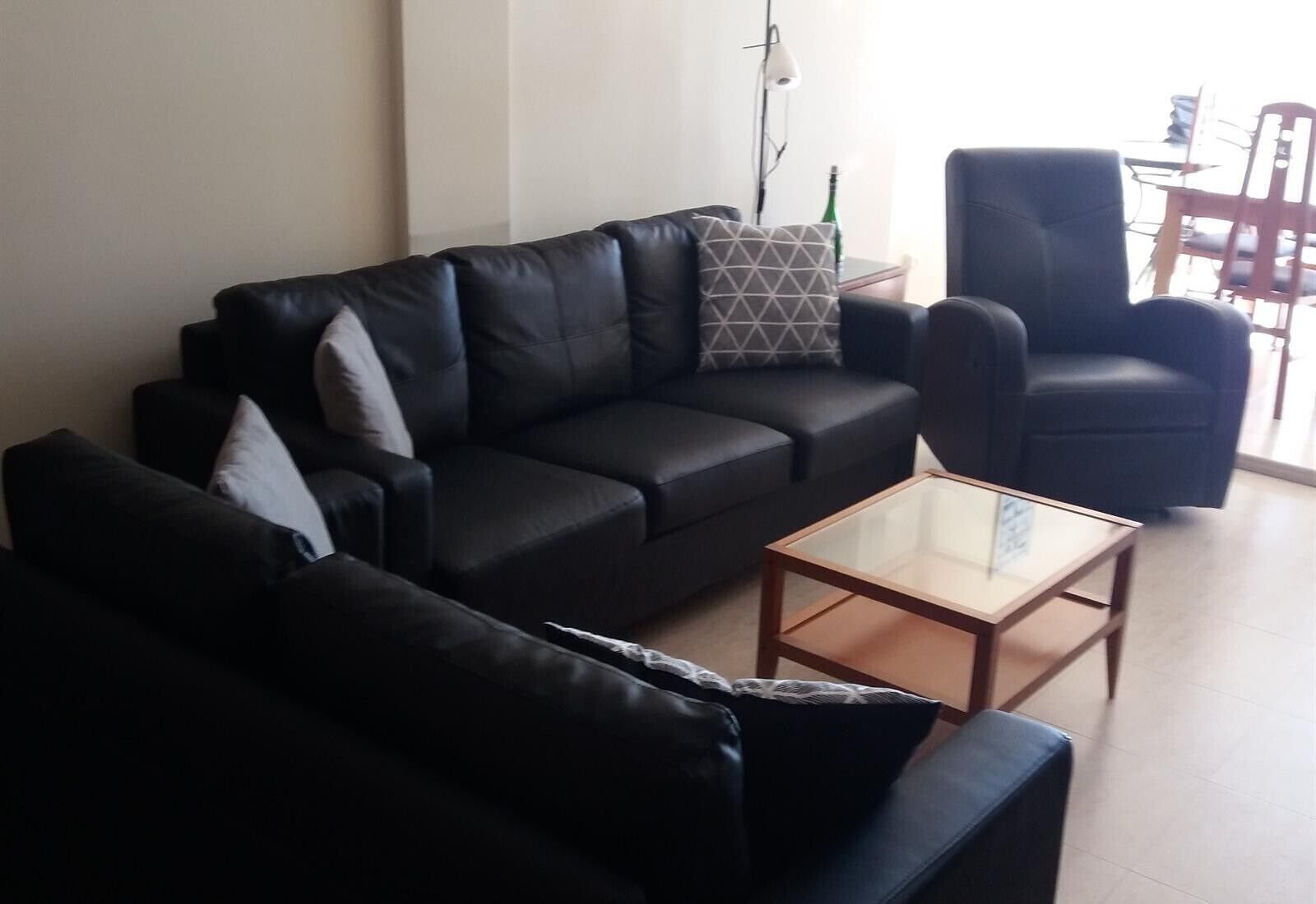 Una sala de estar con un sofá de cuero negro, una mesa de centro de vidrio y un sillón negro.