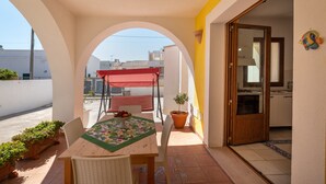 Une terrasse avec une table, des chaises, une petite plante en pot et un auvent rouge.
