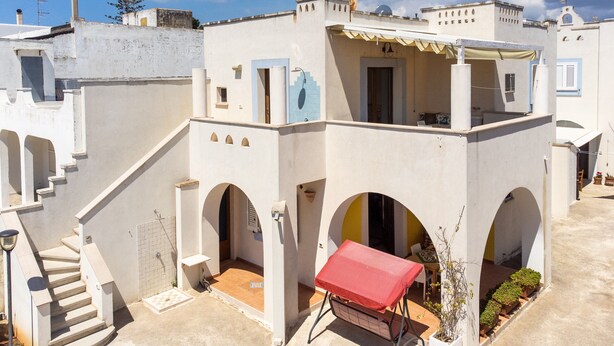 Un bâtiment blanc avec une table rouge, un escalier et un petit espace aménagé en jardin.