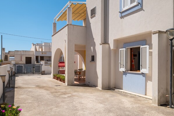 A residential building with a covered patio, a visible door, and a window with shutters.