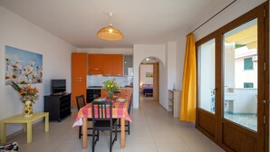 Une cuisine moderne avec des meubles de couleur orange, un coin repas avec une table dressée pour quatre personnes et une grande fenêtre ornée de rideaux jaunes.