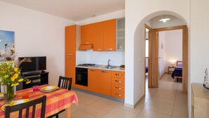 Une cuisine moderne avec des meubles de rangement orange, une table à manger avec des chaises, un téléviseur et un vase rempli de fleurs.