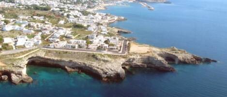 An aerial view of a coastal town with white buildings, a rocky coastline, and clear blue waters.