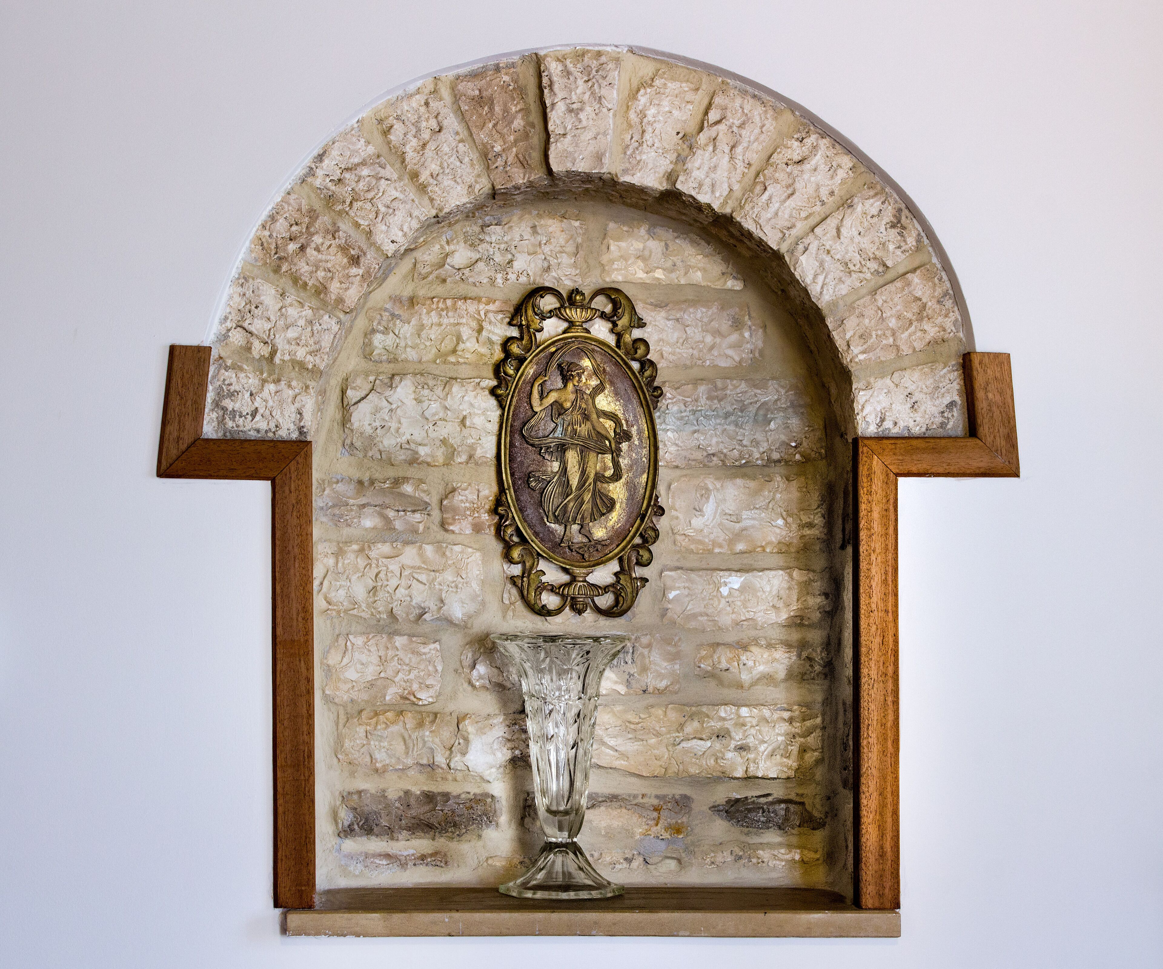A stone-framed niche with a decorative plaque and a clear glass vase.