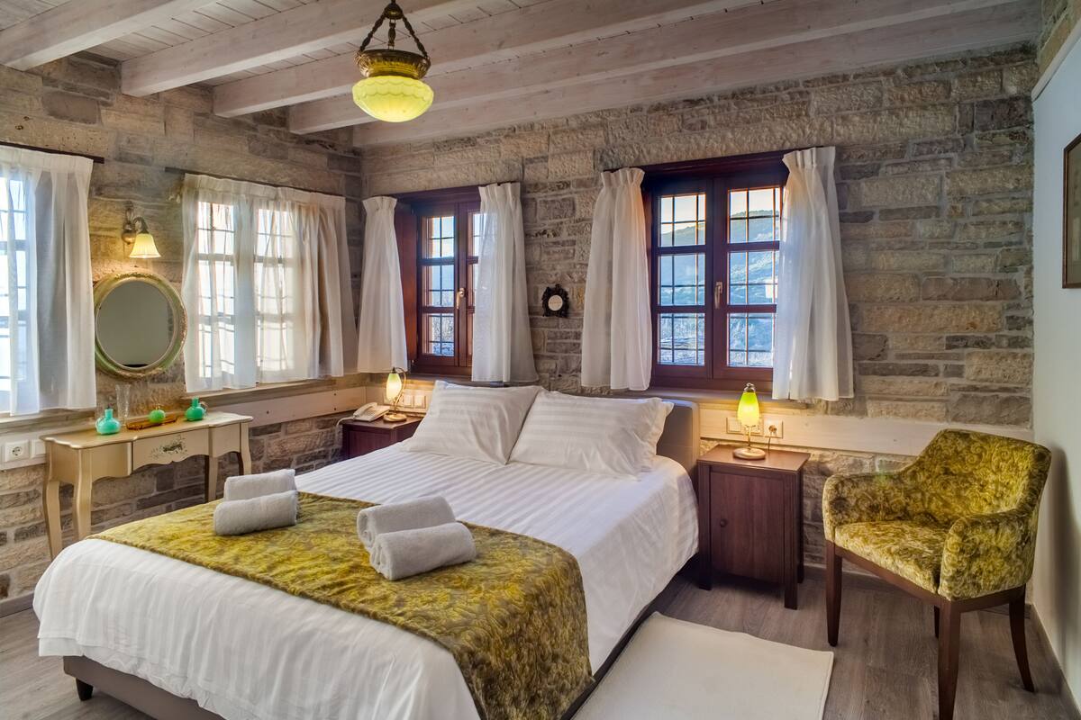 Ein Schlafzimmer mit einem großen Bett, zwei Nachttischen, einem Sessel und einer Steinwand.