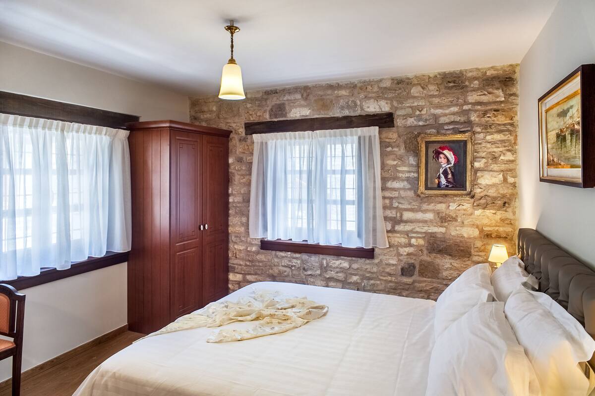 Ein Schlafzimmer mit Steinwand, Holzschrank, Bett mit weißer Bettwäsche und einem Bild an der Wand.