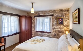 Un dormitorio con pared de piedra, un armario de madera, una cama con ropa blanca y un cuadro en la pared.