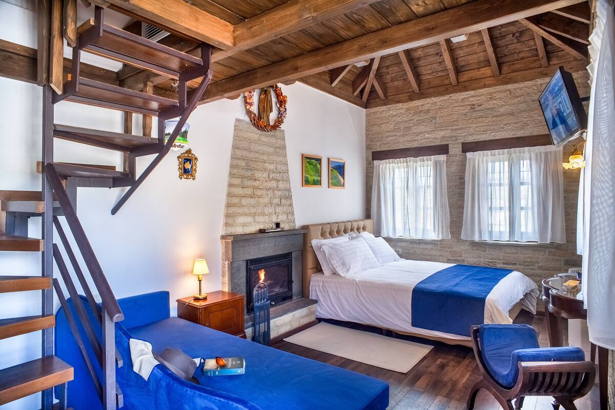 Ein gemütliches Schlafzimmer mit einer Holztreppe, einem Kamin, einem Bett, einem Schreibtisch und einem Fenster mit Vorhängen.