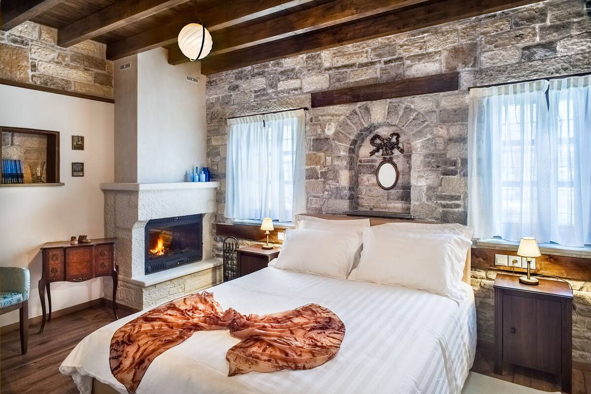 Ein Schlafzimmer mit Kamin aus Stein, einem Bett mit weißen Leinen, einem Nachttisch aus Holz und einer Steinsäule.