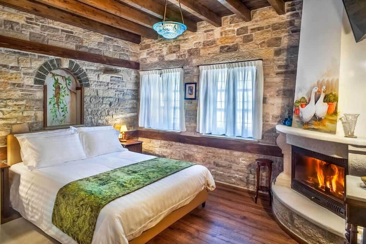 Ein Zimmer mit Steinwand, Kamin, Bett mit grüner Decke und Fenster mit Vorhängen.