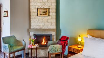 Una habitación acogedora con chimenea, dos sillones, una mesita de noche con lámpara y una cama.
