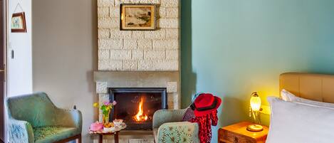 A cozy room with a fireplace, two chairs, a bedside table with a lamp, and a bed.