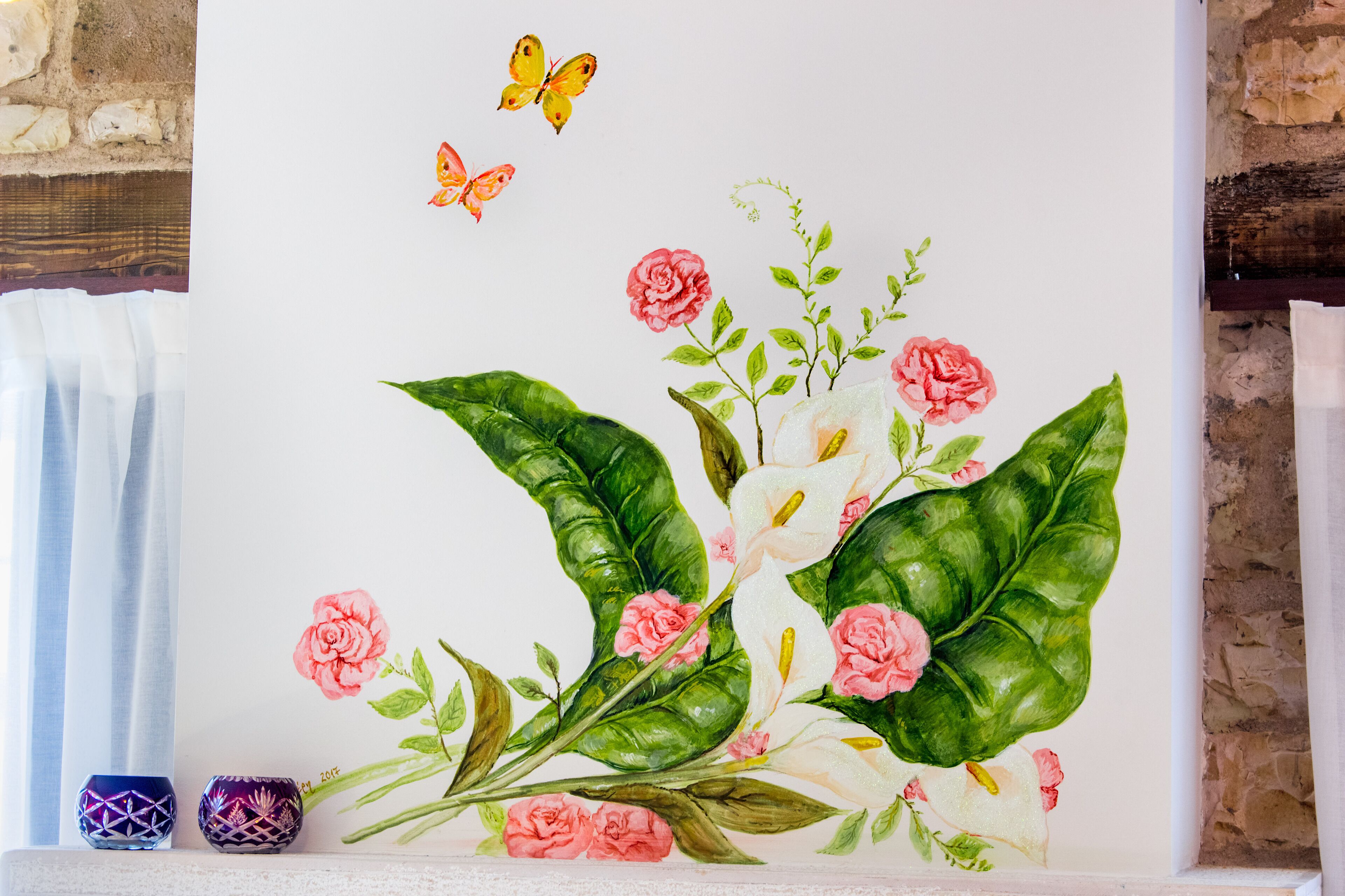 A wall with a floral mural, a butterfly, and two decorative vases.