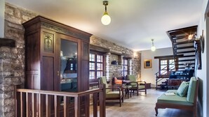 A spacious living area with a wooden staircase, stone walls, and a green sofa. - Gioraldi Art Hotel (Zagori)