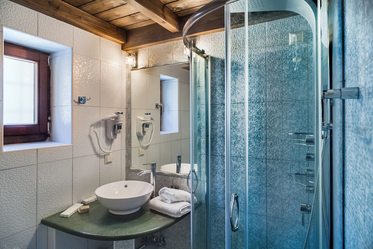 A bathroom with a glass-enclosed shower, a sink with a bowl, and a window above the sink.