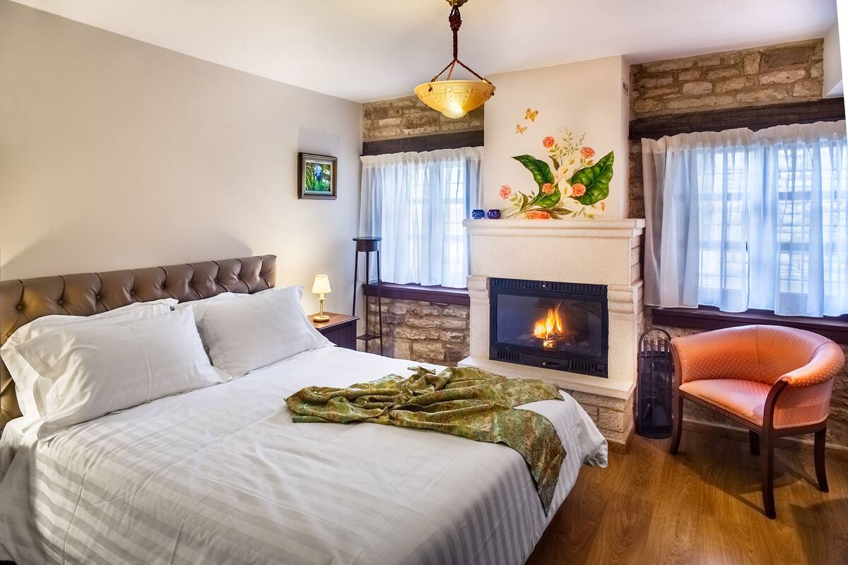 Ein Schlafzimmer mit einem Bett, einem Kamin, einem Sessel und einem Fenster mit Vorhängen.