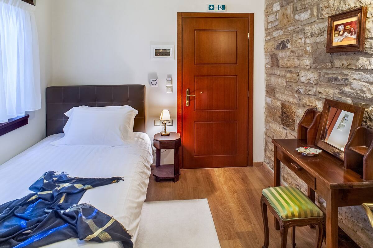 Ein Hotelzimmer mit Bett, Nachttisch, Lampe, einer hölzernen Bank und einer Steinwand.