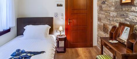 Una camera d'albergo con un letto, un comodino, una lampada, una panca di legno e una parete in pietra.