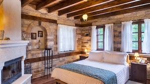 A cozy bedroom with a stone fireplace, a large bed, and two windows with curtains. - Gioraldi Art Hotel (Zagori)