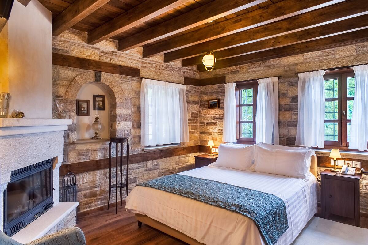 Ein gemütliches Schlafzimmer mit Kamin aus Stein, einem großen Bett und zwei mit Vorhängen versehenen Fenstern.