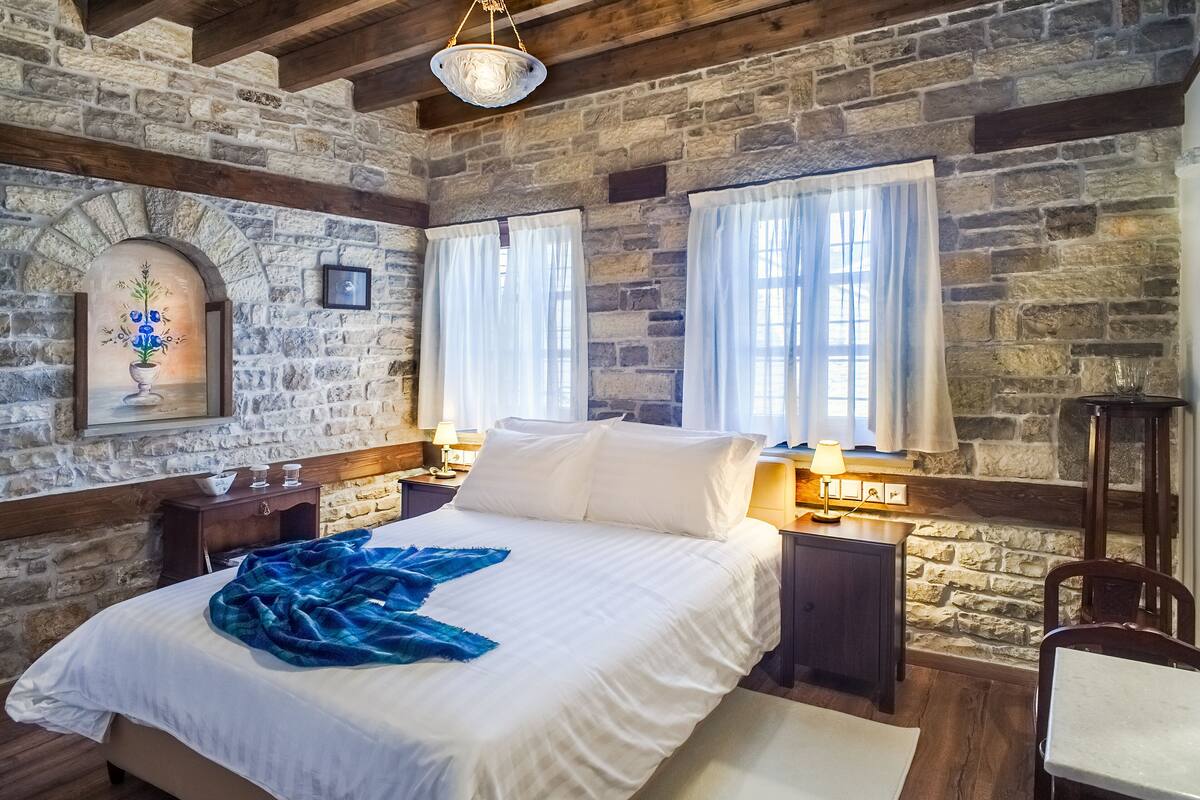 Ein Schlafzimmer mit Steinwand, einem Bett mit weißen Leinen, einer blauen Decke und einem Holzkopfende.