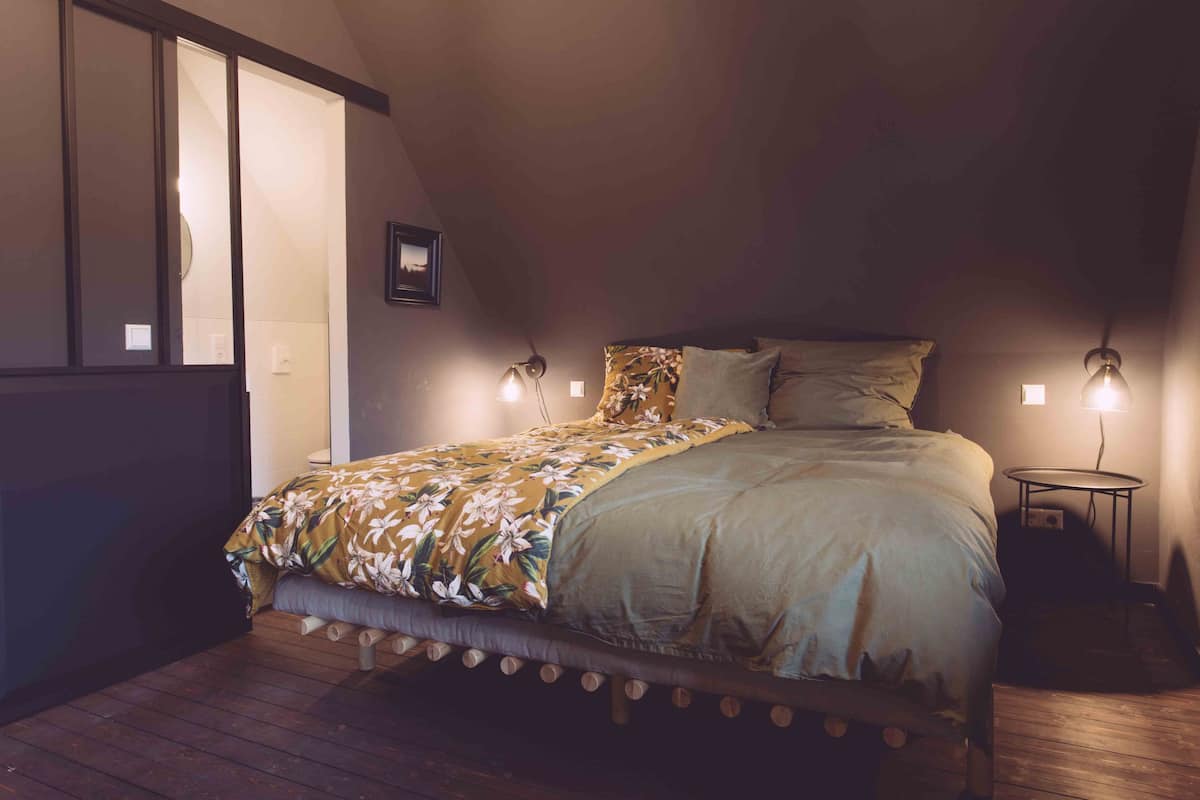 Un dormitorio con una cama, dos lámparas de noche, una mesita y una ventana.