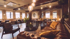 A spacious lounge area with leather sofas, dining tables, and hanging pendant lights. - EDELFUCHS-LODGE (Buehlertal)