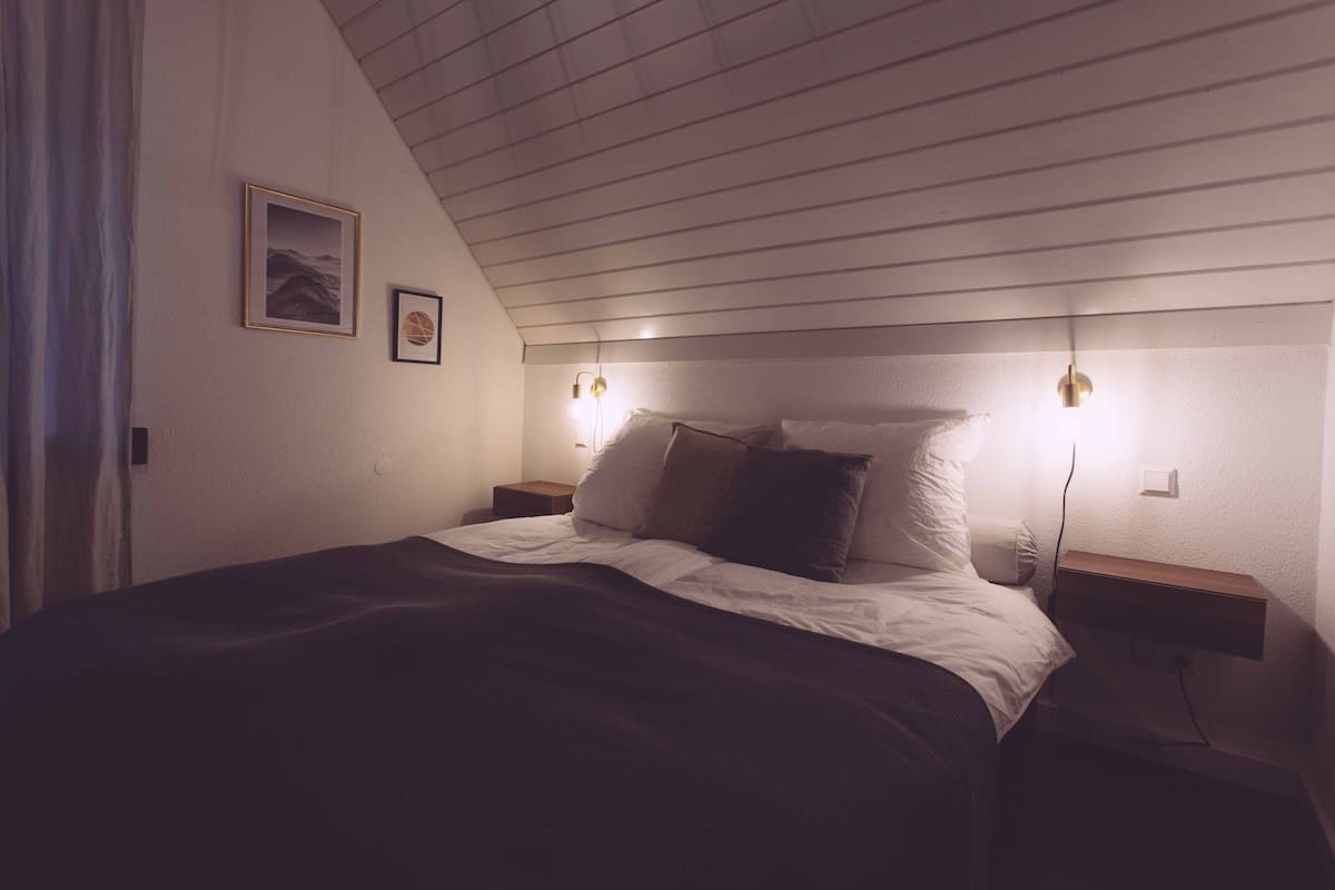 Un dormitorio con una cama, dos mesitas de noche y dos luces fijadas a la pared.