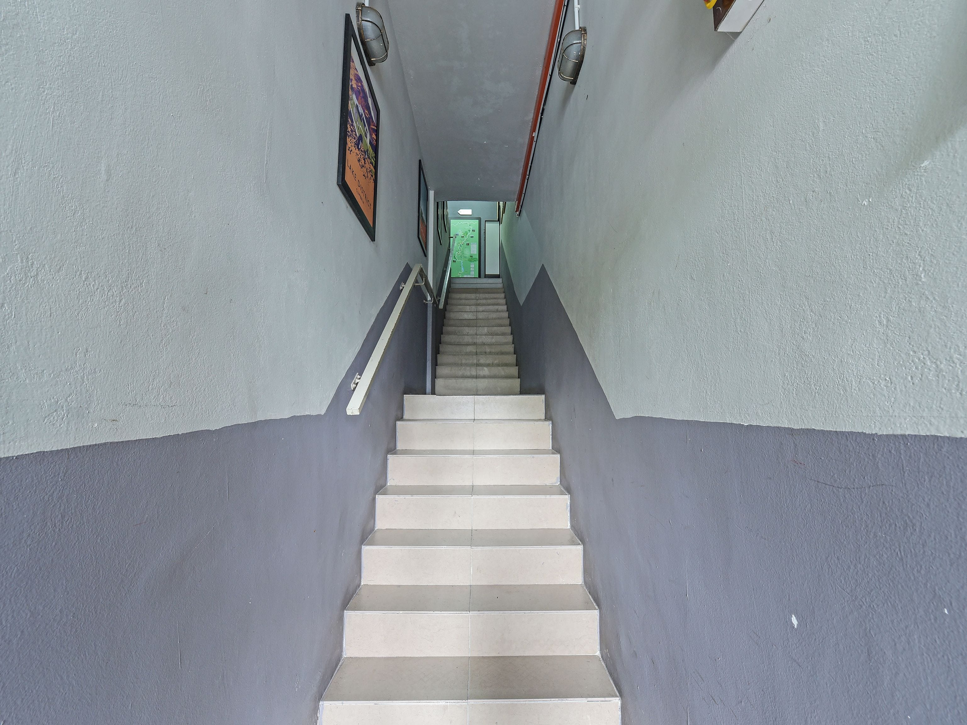 A staircase leading to a door with a green frame, flanked by walls painted in two shades of grey.