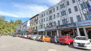 A row of parked cars in front of a building with multiple shops. - Spot ON 90449 Bed Station Guest House Dormitory (Tanah Rata)