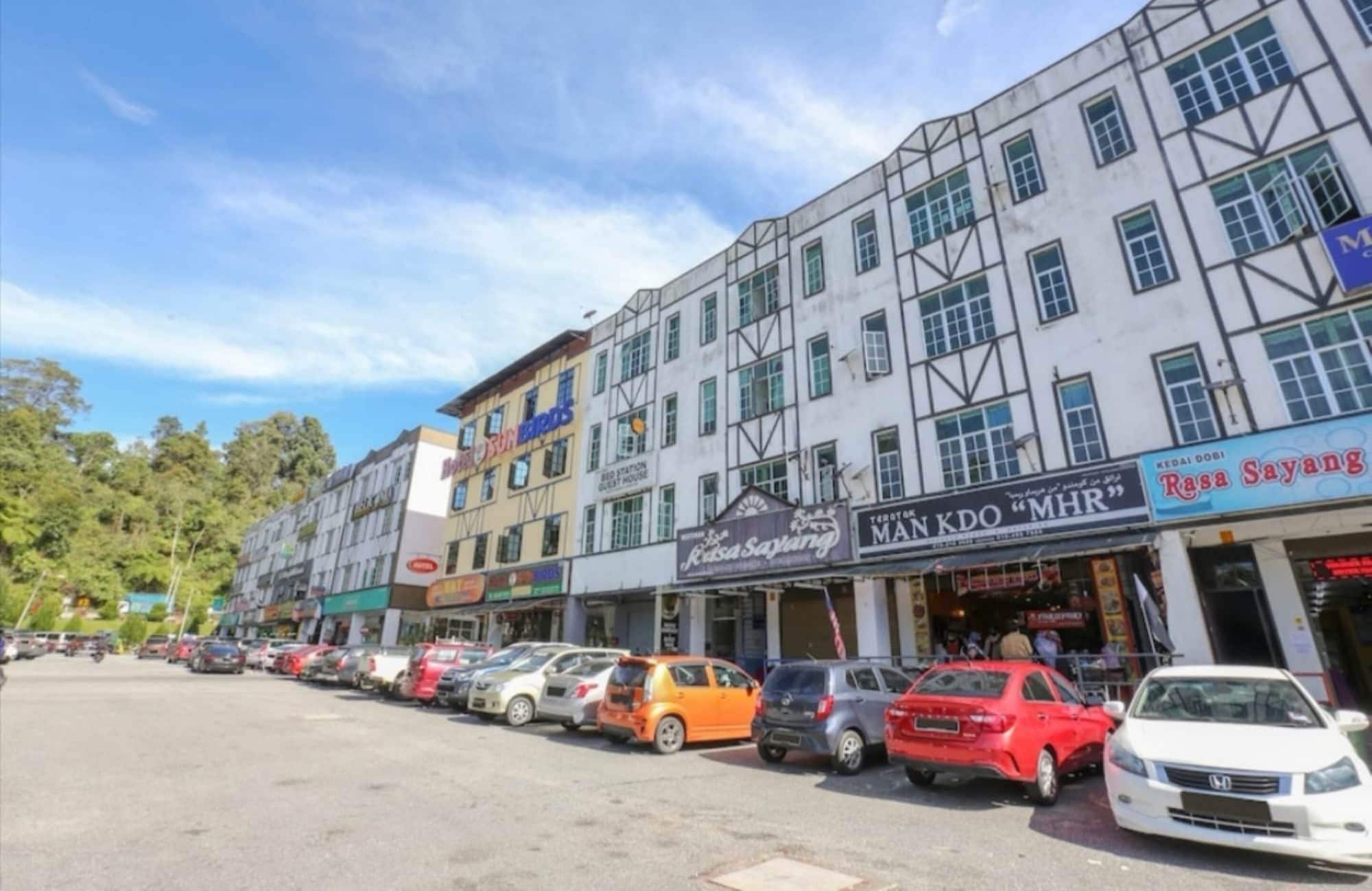 A row of parked cars in front of a building with multiple shops, including a visible sign for 'Rasa Sayang'.