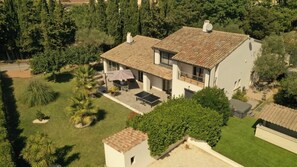 Una casa a due piani con tetto in tegole, un patio con mobili da esterno e un giardino curato.