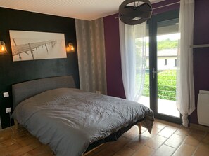 Una camera da letto con un letto, un quadro, una finestra con tende e vista su del verde all'esterno.