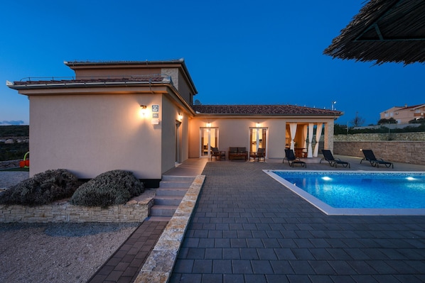 A modern villa with a swimming pool, outdoor seating, and a stone pathway.