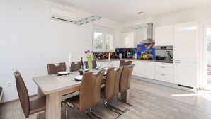 Une cuisine moderne avec des meubles blancs, une table à manger entourée de chaises marron et un four encastré.