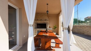 Une terrasse extérieure avec une cheminée en pierre, une table en bois et des rideaux blancs.