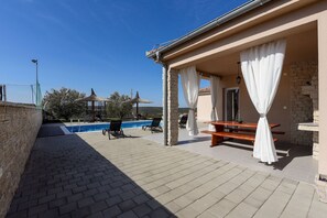 A covered outdoor area with a pool, lounge chairs, and a table. - Villa Bašić (Sukosan)