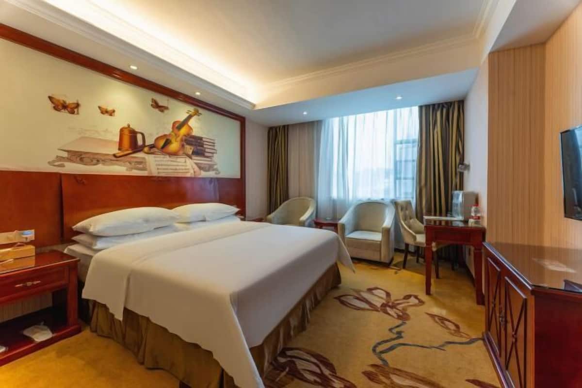 A hotel room with a large bed, two bedside tables, a desk, a chair, and a TV.