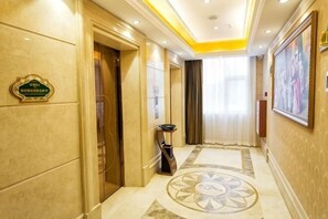 A hotel corridor with a marble floor, a door with a sign, a trash bin, and a framed picture on the wall. - Vienna Hotel (Ji'an Railway Station) (Ji'an)