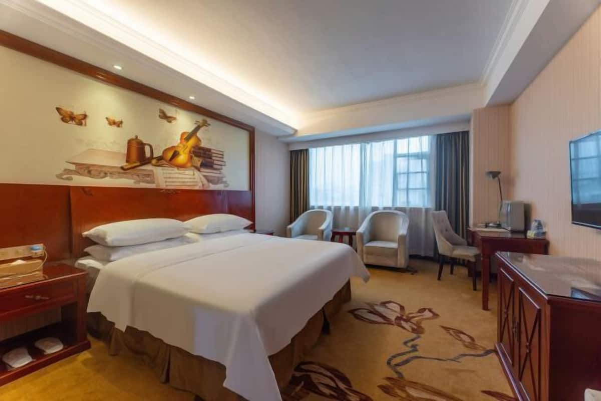 A hotel room with a large bed, two chairs, a desk, a TV, and a wall with a butterfly mural.