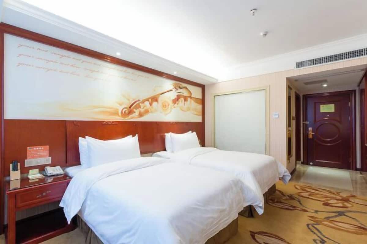 A hotel room with two beds, a wooden headboard, a nightstand with a phone and a small table, and a large wall mural.