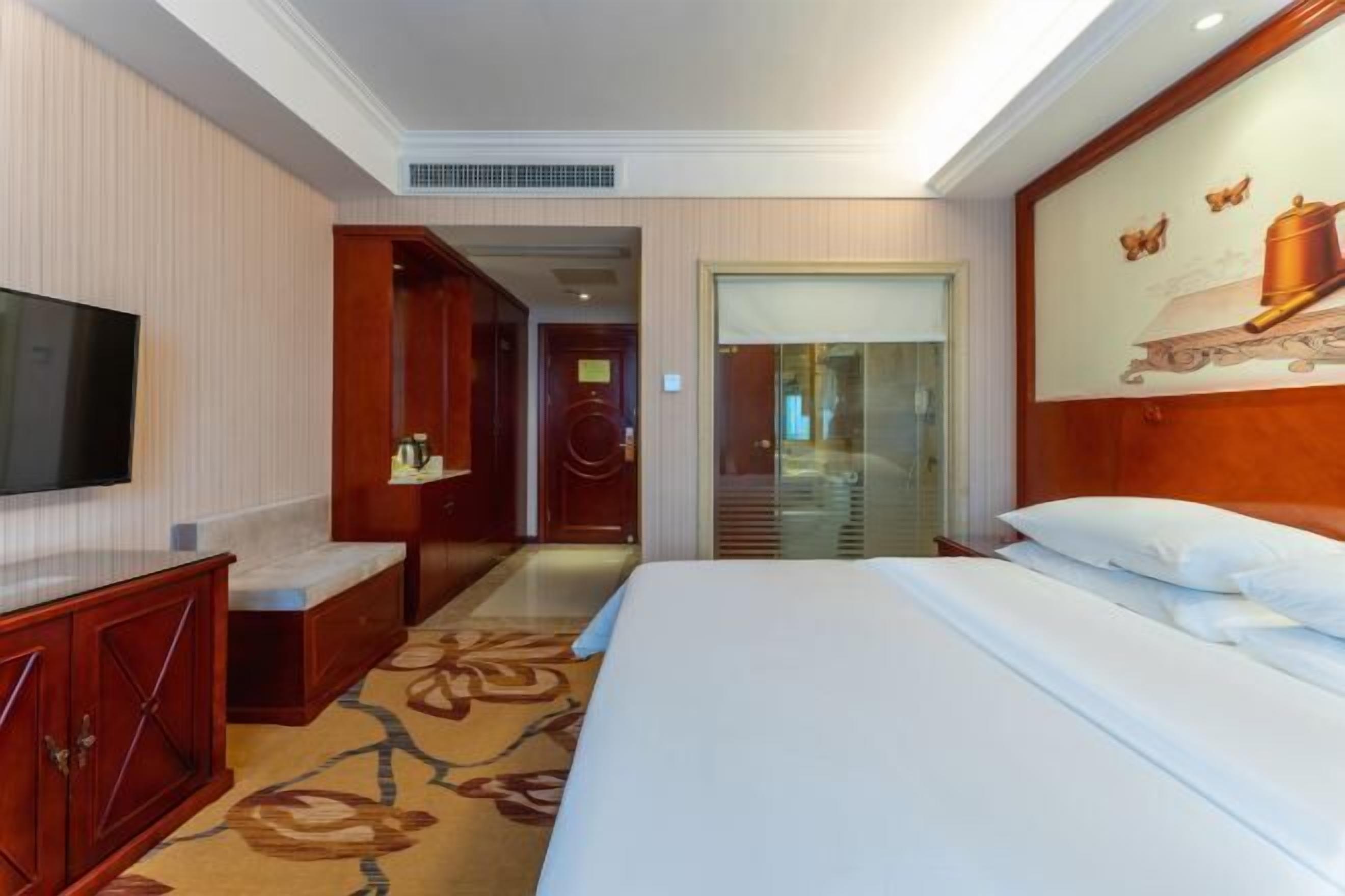 Una habitación de hotel con cama, televisión, escritorio y un cuadro en la pared.